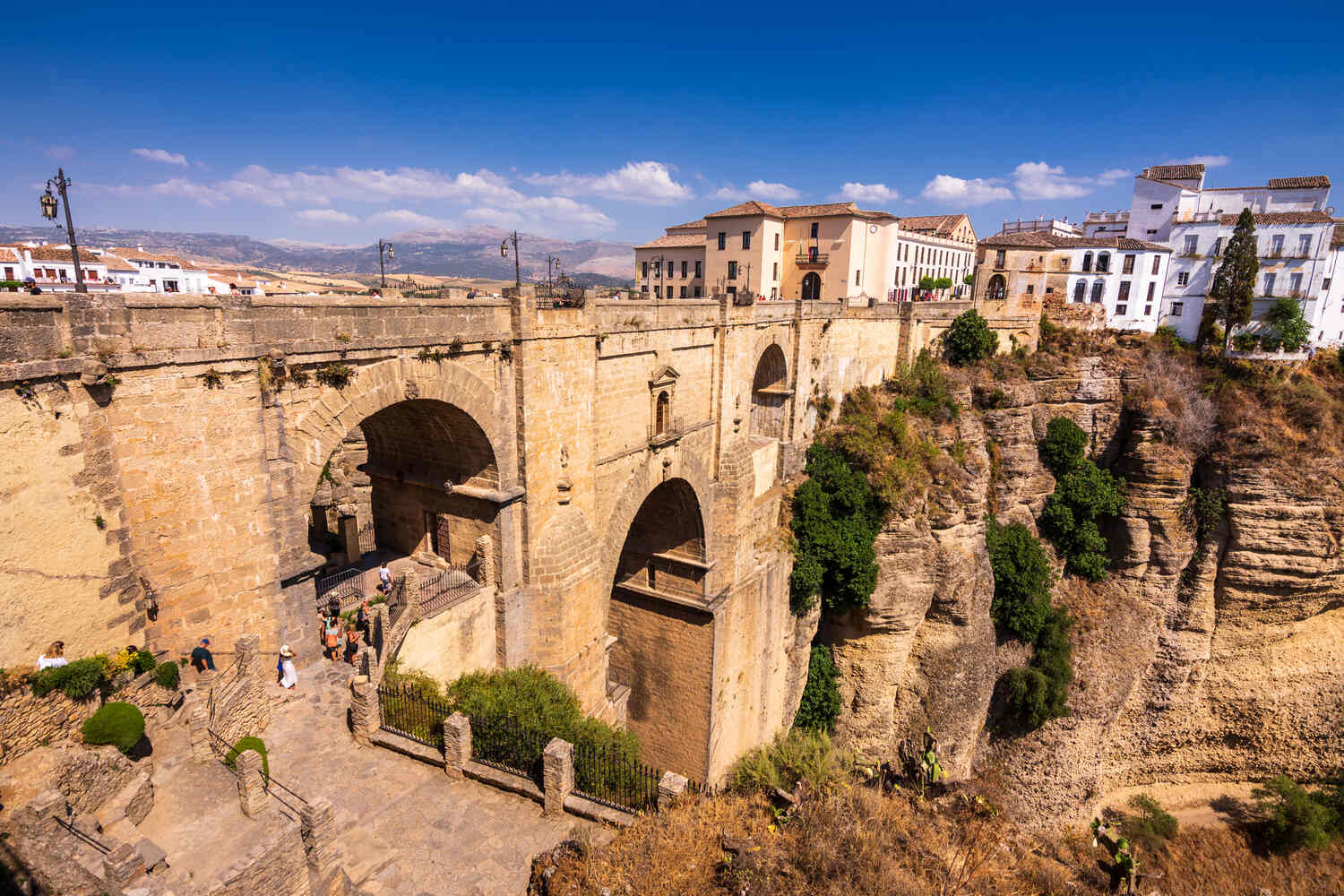 View of Ronda's Puente Nuevo bridge spanning a deep gorge under a clear sky.