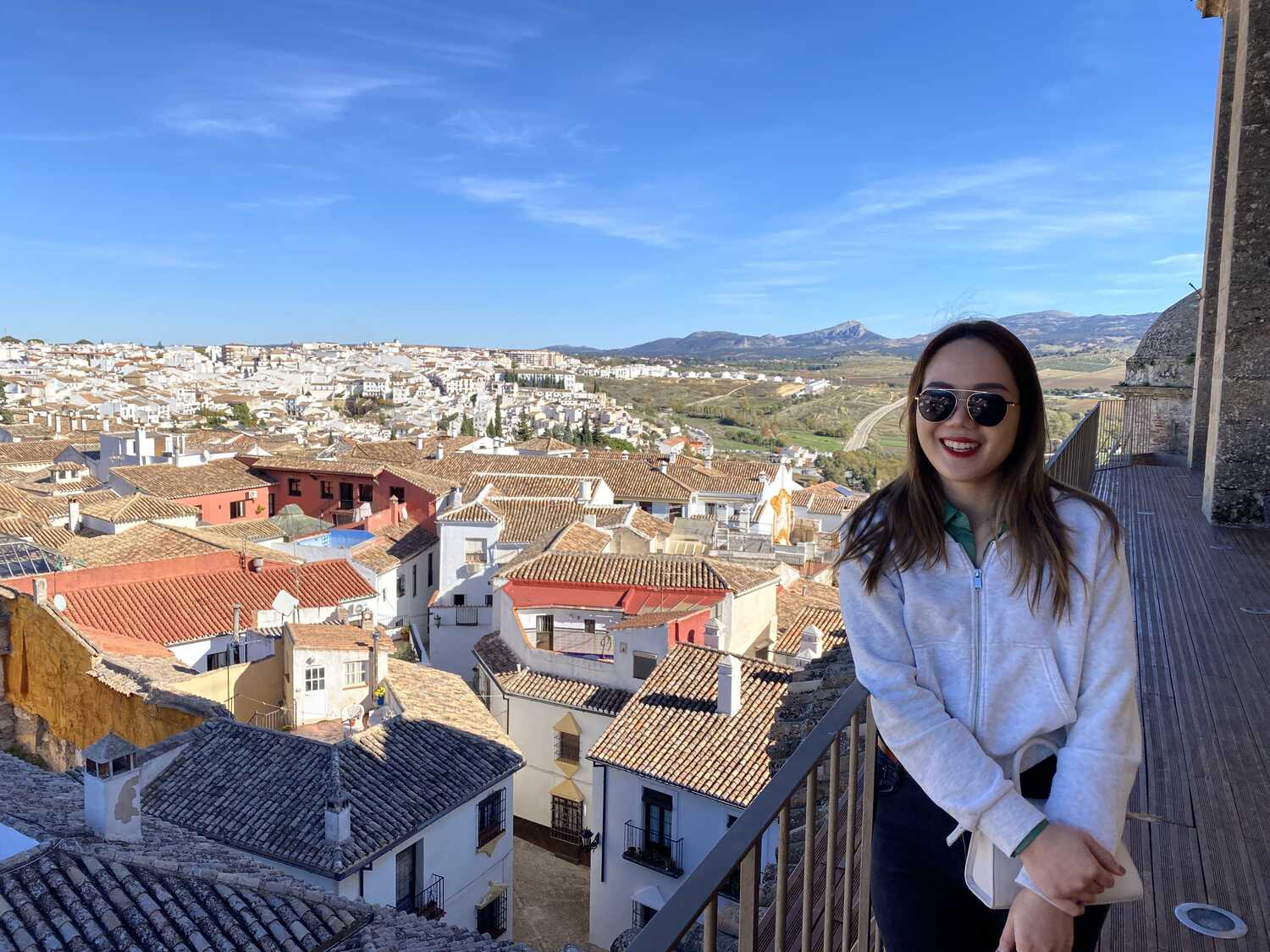 Woman smiling on a balcony overlooking the white houses and hills of Ronda, Spain.