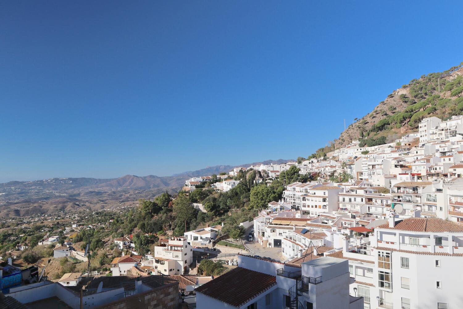 A panoramic view of a hillside town with white buildings and terracotta roofs under a clear blue sky