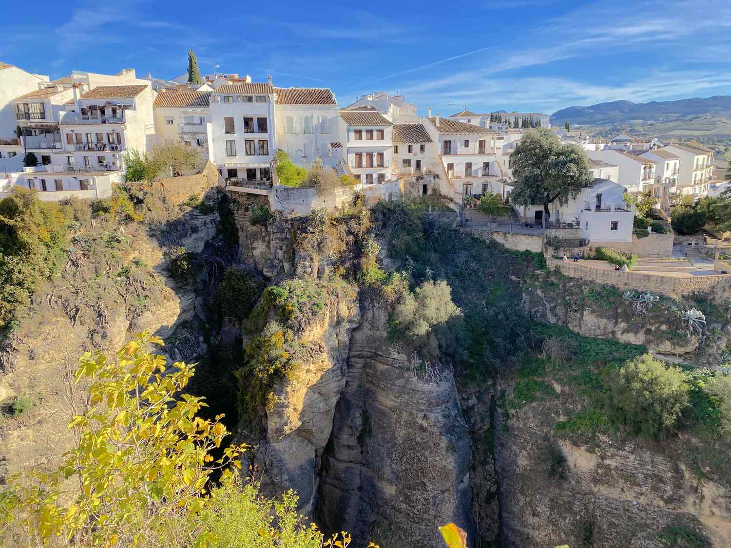 day-trip-from-seville-to-ronda, A whitewashed town perched on the edge of a steep cliff with buildings overlooking a canyon.