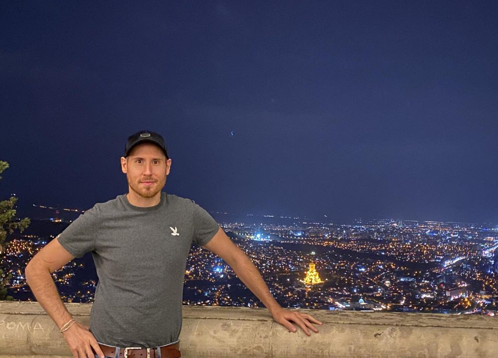 Man posing with a night view of Tbilisi from above.